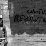 little boy standing in front of a brick wall with words Culture Revolution spray painted on it