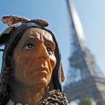 Upclose shot of the head of a toy figurine of a man in traditional Indian attire in foreground with Eiffel Tower in background