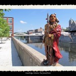 Toy figurine of Indian man in traditional dress and wrapped in red robe in foreground, river and old city buildings in backround