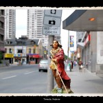 Toy figurine of Indian man in traditional dress and wrapped in red robe in foreground, urban street scene in background