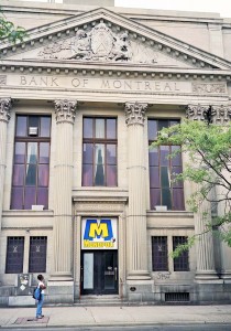 large stone facade pf a former bank building with classical architectural elements and a frieze at the top that shows the carvings that include an Indian man in traditional dress