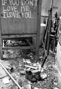 a back alley with wood bits, garbage, old pair of shoes and a cabinet with the words If you don't love me I love you spray painted on it.