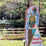 wooden cutout of Indian figure with headdress and hole for someone to put their face in, sign on the cutout reads Gifts and Ryan's Campsite